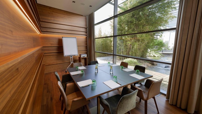 Modern meeting room with wooden walls, large table and view of a garden.