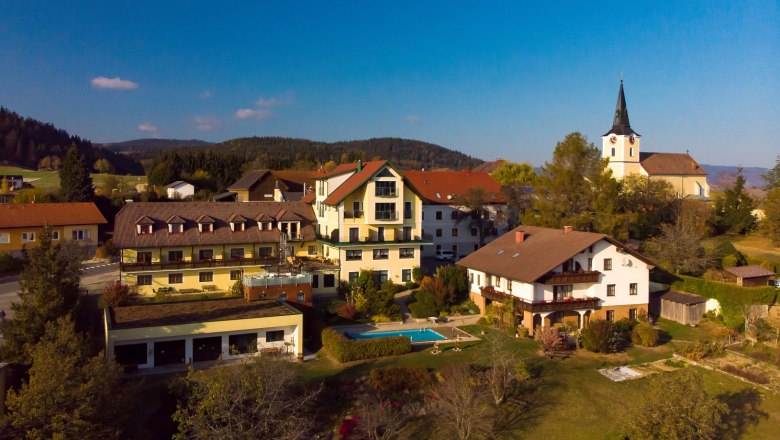 Aerial view of a village with a hotel, a pool and a church in the background.