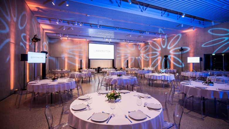 Elegant function room with round, laid tables and modern lighting.