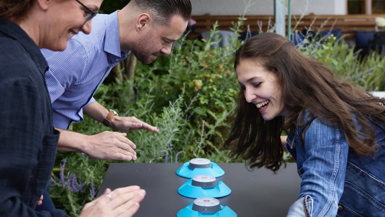 Three people play an outdoor reaction game with blue buttons.