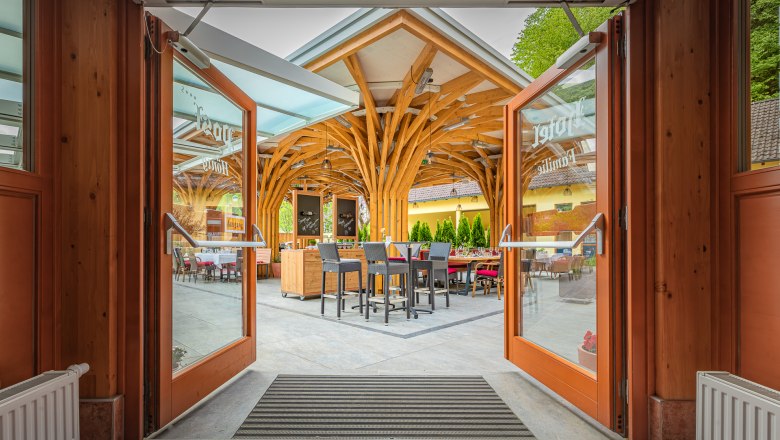 Open glass doors lead to a terrace with a wooden roof and seating.