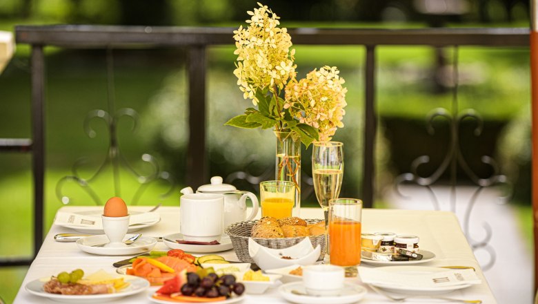 Breakfast table on the terrace with flowers, juice, bread rolls and eggs.