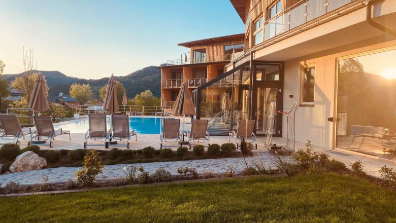 Outdoor area of the Naturhotel Molzbachhof with pool and sun loungers at sunset.