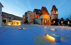 Evening shot of the illuminated BURG Perchtoldsdorf with modern forecourt and benches.