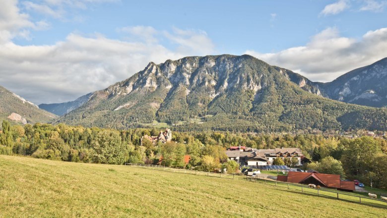 A panoramic view of a mountainous landscape with meadows in the foreground and a village in the background.