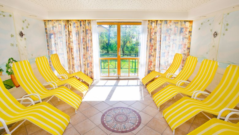 Bright sauna area with yellow and white striped loungers and large windows.