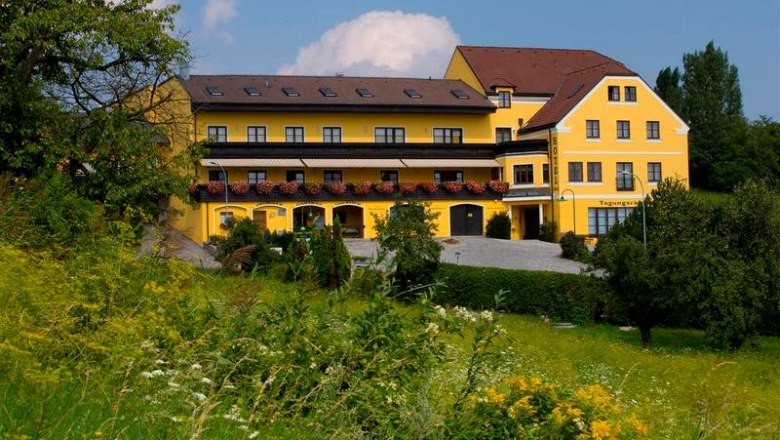 Yellow hotel building with flower balconies, surrounded by green landscape.