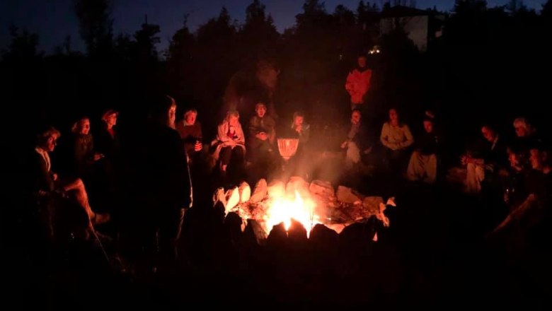 People sit in a circle around a campfire at night.