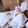 Two people in bathrobes have breakfast in bed with champagne and dessert.