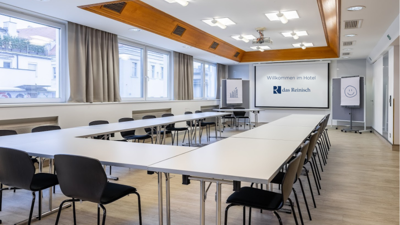 Seminar room at Das Reinisch Hotel with tables, chairs and presentation screen.