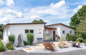 Modern, white building with garden and gravel path, blue sky in the background.