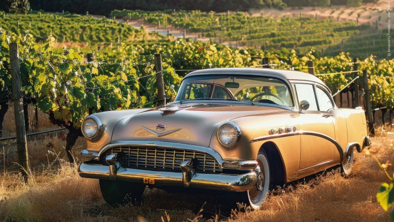 A golden vintage car stands in a sunny vineyard.