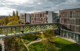 Modern hotel building with glass bridge and garden.