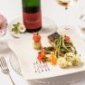 Elegant dish with fish, asparagus and potatoes on a white plate, decorated with flowers. A bottle of wine and a glass in the background.