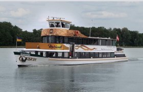 An excursion boat named MS Mariandl sails on a river surrounded by trees. It carries the flags of Ukraine and Austria.