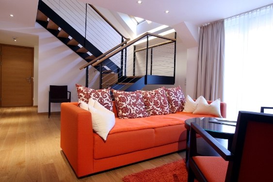 Modern suite with orange couch, decorative cushions and staircase in the background.