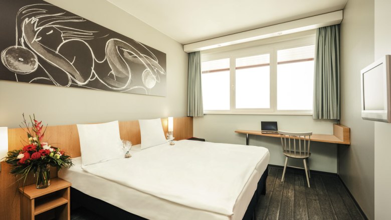 Modern double room with large bed, artwork on the wall, desk and flower arrangement.