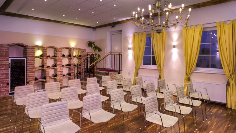 A conference room with white chairs, yellow curtains and a chandelier.