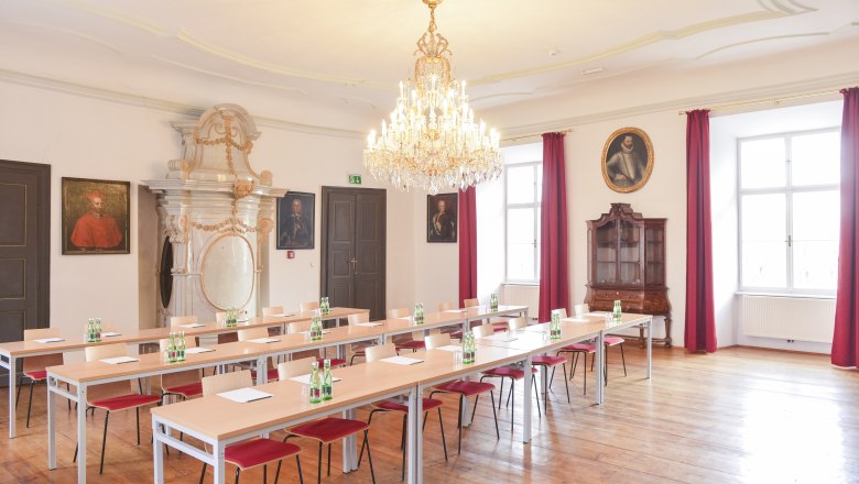 Elegant seminar room with chandelier, wooden floor and portraits on the walls.