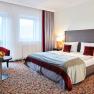 Double room at Hotel Schneeberghof with double bed, red pillows, table with fruit bowl and two armchairs.
