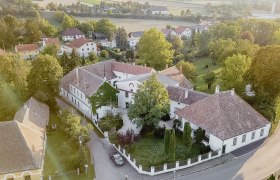 Aerial view of a historic building complex with courtyard, surrounded by trees and other houses in a rural area.