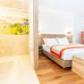 Modern hotel room with double bed, orange armchair and open shower.