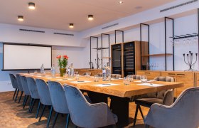 Modern conference room with large wooden table, gray chairs and presentation screen.