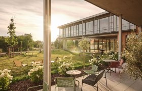 A modern patio with patio furniture and flowers in front of a building at sunset.