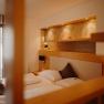 A cozy apartment with a double bed and a balcony door. Part of the wall is paneled with light-colored wood; behind the bed is a recessed niche with a shelf and spotlights, painted in an earthy gold.