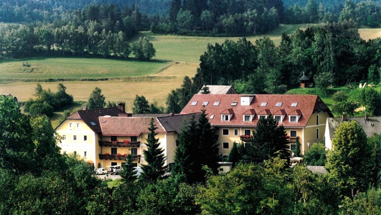 A large building with red roofs in a green, wooded landscape.