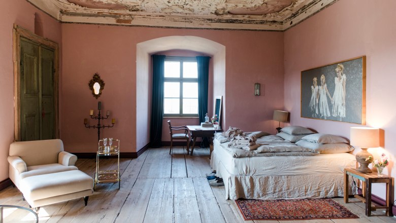Elegant bedroom with antique ceiling, pink walls and wooden floor.