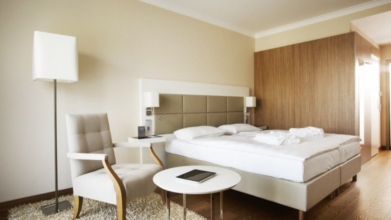 Modern hotel room with double bed, armchair, table and floor lamp.