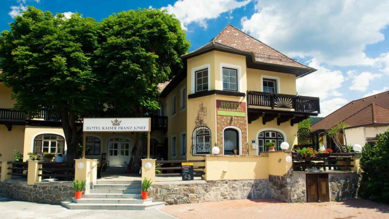 Entrance to the Hotel Kaiser Franz Josef with yellow façade and balcony.