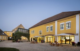 Yellow building with courtyard and outdoor tables at dusk.