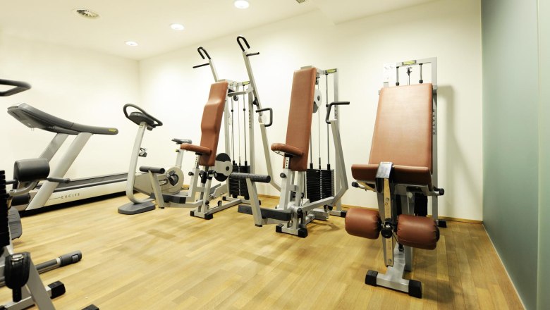 A fitness room with treadmill, exercise bike and strength equipment on a wooden floor.