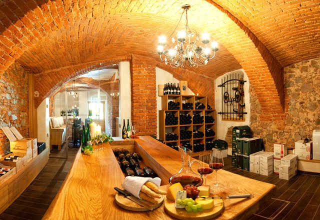 A cozy wine cellar with brick walls, a wooden table, shelves of wine bottles and a plate of cheese and grapes.