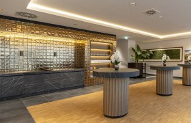 Modern room for seminar coffee breaks with a golden wall, black marble tables and orchids.