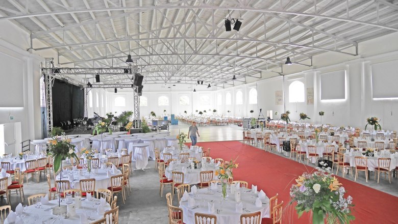 Interior view of a large hall with gala seating, round tables and a stage.