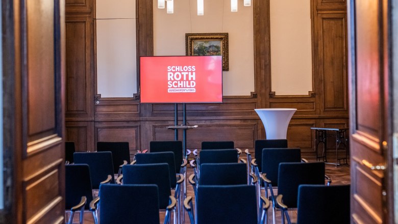 A seminar room in Rothschild Castle with rows of chairs, a screen and a high table.