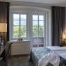 A cozy hotel room with double bed, window with mountain view, desk and flowers.