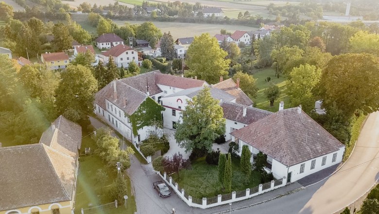 Aerial view of a historic building complex with courtyard, surrounded by trees and other houses in a rural area.