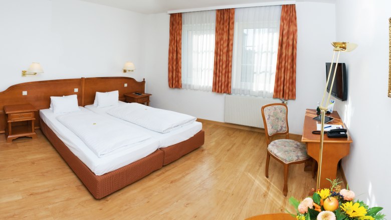 A cozy double room with two beds, wooden furniture and a desk with chair.