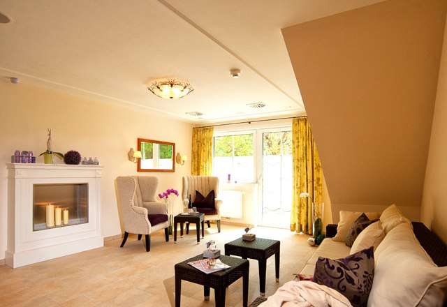 A cozy wellness relaxation area with fireplace, armchairs, sofa and small table, decorated with candles and plants.