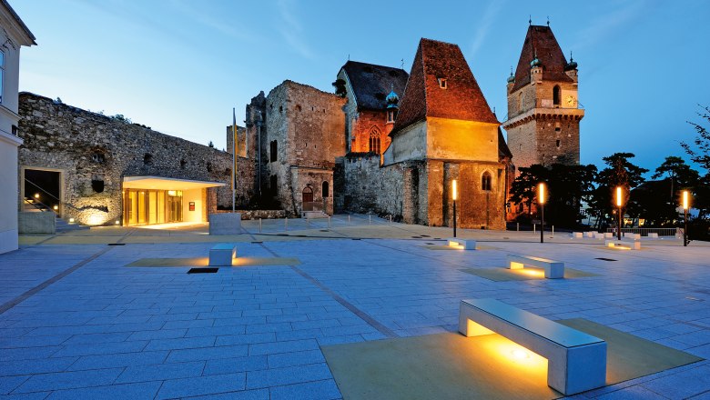Evening shot of the illuminated Perchtoldsdorf Castle with modern forecourt and benches.