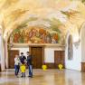 Interior view of a magnificent room in G&ouml;ttweig Abbey with frescoes on the ceiling and three people talking.