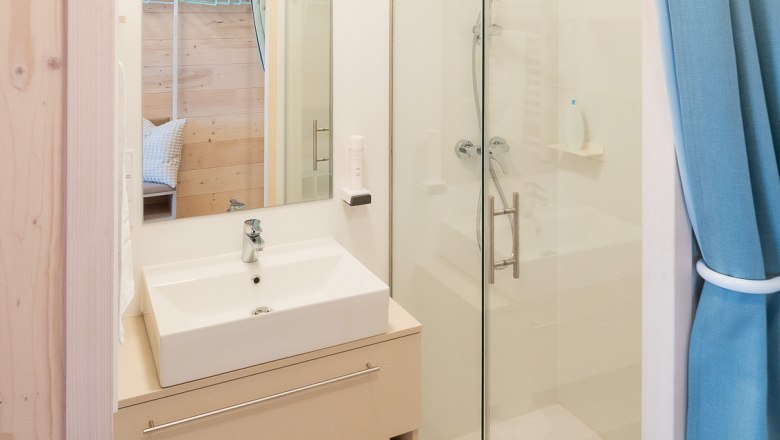 Modern bathroom with washbasin, mirror, shower and blue curtains.