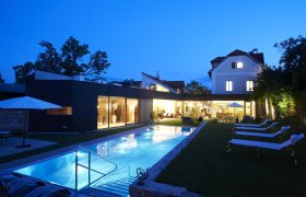 Evening view of a modern hotel with illuminated pool and sun loungers in the garden.