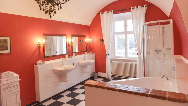 Elegant bathroom with red walls, two washbasins, bathtub, shower and chandelier.