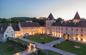 Aerial view of Walpersdorf Castle at dusk, illuminated with guests at a garden party in the courtyard.