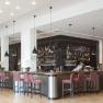 Modern hotel bar with red chairs and black hanging lamps.